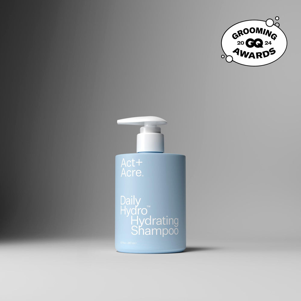 A light blue pump bottle of Act+ Acre. Daily Hydro Hydrating Shampoo on a dark gray to light gray gradient background, featuring a Grooming Awards 2024 badge in the top right corner.