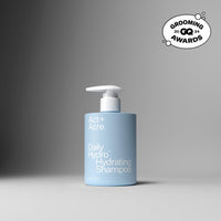 A light blue pump bottle of Act+ Acre. Daily Hydro Hydrating Shampoo on a dark gray to light gray gradient background, featuring a Grooming Awards 2024 badge in the top right corner.